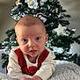 baby, infant, christmas_tree, holiday, ornaments, lights, blanket, knitted, red_clothing, white_clothing, face, eyes, hand, home_interior, festive, decoration, person, portrait, cute, seasonal