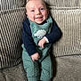 baby, smiling, sitting, couch, green_overall, sheep_design, socks, happy, infant, cute, face, child, indoors, texture, cozy, blue_eyes, clothing, person, portrait, furniture