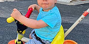 Milan participe au concours pour gagner de l'argent avec cette photo : toddler, child, tricycle, outdoor, cap, shorts, blue_tshirt, toy, playground, vehicle, sidewalk, urban, daylight, face, person, curious, hand, footwear, casual_clothing, summer