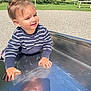 toddler, child, striped_sweater, metal_slide, playground, outdoor, sunlight, grass, gravel, park, young_child, casual_clothing, smiling, hands, face, daylight, recreation, fun, person, cute