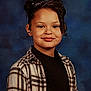 child, portrait, smile, curly_hair, plaid_shirt, black_top, school_photo, blue_background, young, person, face, hair_buns, casual_clothing, studio, indoor, happy, cute, posing, head_and_shoulders, childhood