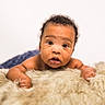 baby, infant, child, portrait, face, wide_eyed, curly_hair, lying_down, blanket, fluffy, cream_colored, indoor, studio, close_up, looking_at_camera, arms, hands, soft_lighting, adorable, photography