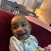 Nicole joined the competition — help win amazing prizes! baby, child, smile, happy, infant, onesie, floral_pattern, cushion, red, crib, bedroom, lamp, mirror, window, curtains, indoor, person, furniture, lighting, cozy