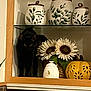 black_cat, cat, kitchen, decor, sunflowers, ceramic_jars, pumpkin, flowers, shelf, shadow, wood_frame, tile, indoor, plant, animal, pet, dark, cozy, still_life, ninja_cat