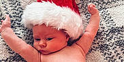 Willow joined the competition — help win amazing prizes! baby, infant, santa_hat, carpet, floor, bare_chest, diaper, cute, holiday, christmas, red_hat, white_fur, skin, child, lying_down, arms_up, indoors, soft_texture, cozy, portrait