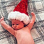 baby, infant, santa_hat, carpet, floor, bare_chest, diaper, cute, holiday, christmas, red_hat, white_fur, skin, child, lying_down, arms_up, indoors, soft_texture, cozy, portrait