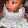 Whiyn'Ter is registered to the contest to win money with this photo: baby, child, dress, white_dress, red_bow, sitting, curious, indoors, couch, foot, portrait, face, skin, hair, happy, cute, infant, one_person, young_child, headwear
