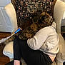 blanket, casual, cat, chair, comfort, cozy, curled_up, furniture, home, indoor, leggings, patterned_blanket, person, phone, relaxing, resting, socks, sweater, tortoiseshell_cat, wooden_floor