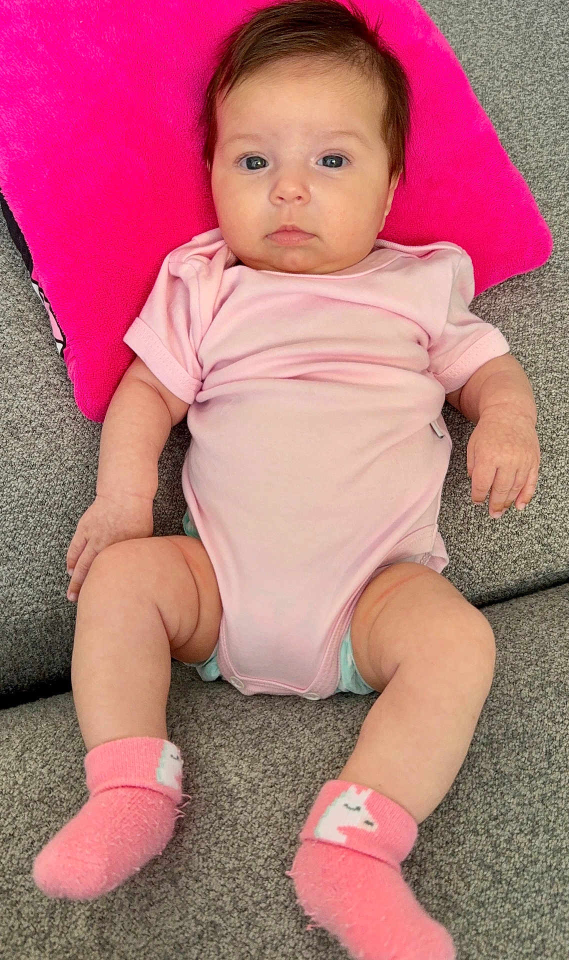 Mila joined the competition — help win amazing prizes! baby, infant, onesie, socks, pink_pillow, pink_clothing, couch, carpet, portrait, looking_at_camera, cute, chubby, newborn, head, hands, legs, diaper, soft_texture, indoor, relaxed
