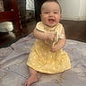 baby, child, smiling, yellow_dress, sitting, indoor, blanket, happy, person, floor, wooden_floor, furniture, babygirl, cute, infant, clothing, portrait, face, expression, playful