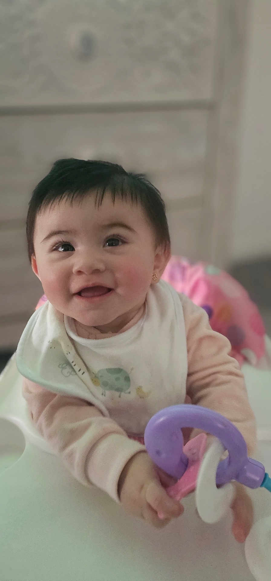 Gianna Broquis is registered to the contest to win money with this photo: baby, child, smiling, toy, high_chair, face, hand, clothing, bib, earring, indoor, cute, person, happy, infant, pink, purple, playful, portrait, young