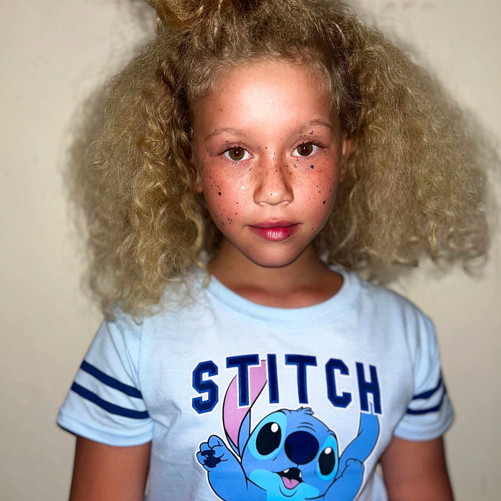 Jazlynn is registered to the contest to win money with this photo: blue_clothing, cartoon_character, casual, child, curly_hair, expression, eyes, face, freckled_face, freckles, hairstyle, indoor, lips, person, portrait, skin, stitch, top_bun, tshirt, young
