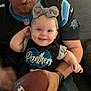 Ivy is registered to the contest to win money with this photo: baby, child, smiling, football, headband, bow, panthers, shirt, jersey, adult, arm, watch, indoor, couch, happy, person, sports, team, black_clothing, casual