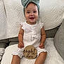 baby, infant, smiling, headband, bow, white_clothing, sitting, blanket, couch, texture, happy, child, indoors, cute, portrait, young_child, wooden_sign, eight_months, person, comfortable