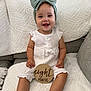 Avery is registered to the contest to win money with this photo: baby, infant, smiling, headband, bow, white_clothing, wooden_sign, eight_months, couch, blanket, indoor, happy, child, portrait, sitting, cute, home, texture, person, young_child