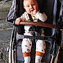 Leão participe au concours pour gagner de l'argent avec cette photo : baby, infant, child, stroller, pram, seatbelt, smiling, hand_in_mouth, socks, patterned_pants, brown_handle, fabric_seat, metal_frame, concrete_ground, outdoor, portrait, cute, happy, face, eyes