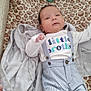 baby, infant, playpen, blanket, leopard_print, clothing, suspenders, shirt, text_on_clothing, baby_sock, gray_blanket, face, person, lying_down, indoor, cute, young_child, soft_texture, cozy, baby_brother
