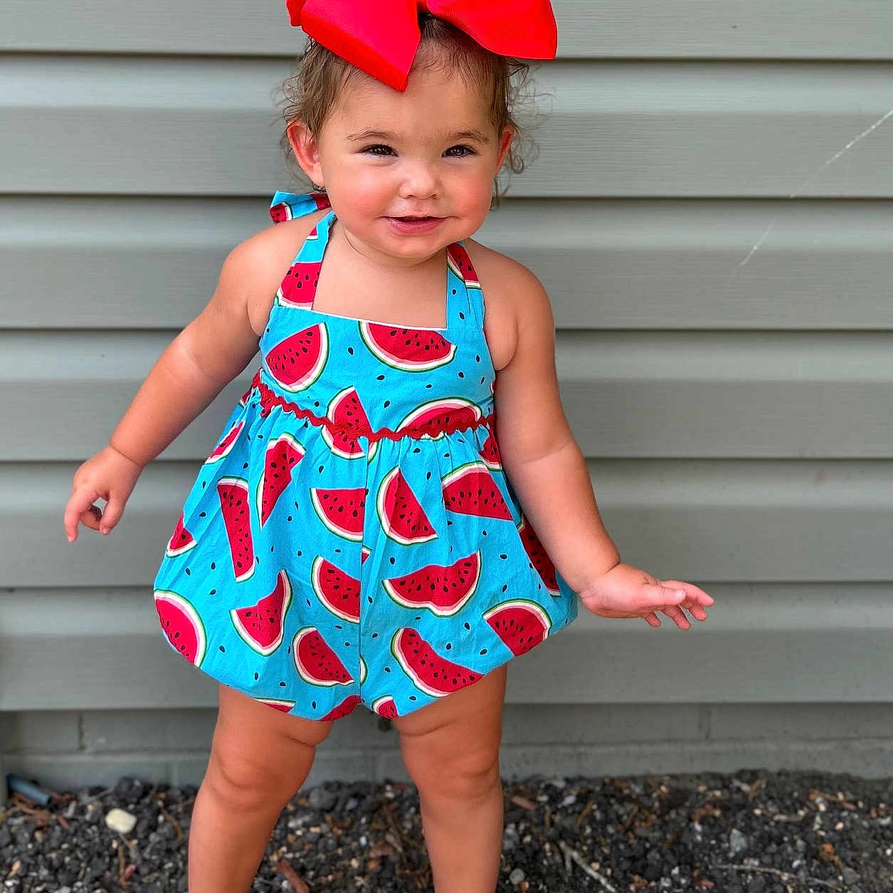 Karlieanne is registered to the contest to win money with this photo: blue_romper, child, cute, fashion, gravel, gray_siding, happy, headwear, outdoor, person, playful, portrait, red_bow, sandals, smiling, standing, summer, toddler, watermelon_pattern, young_child