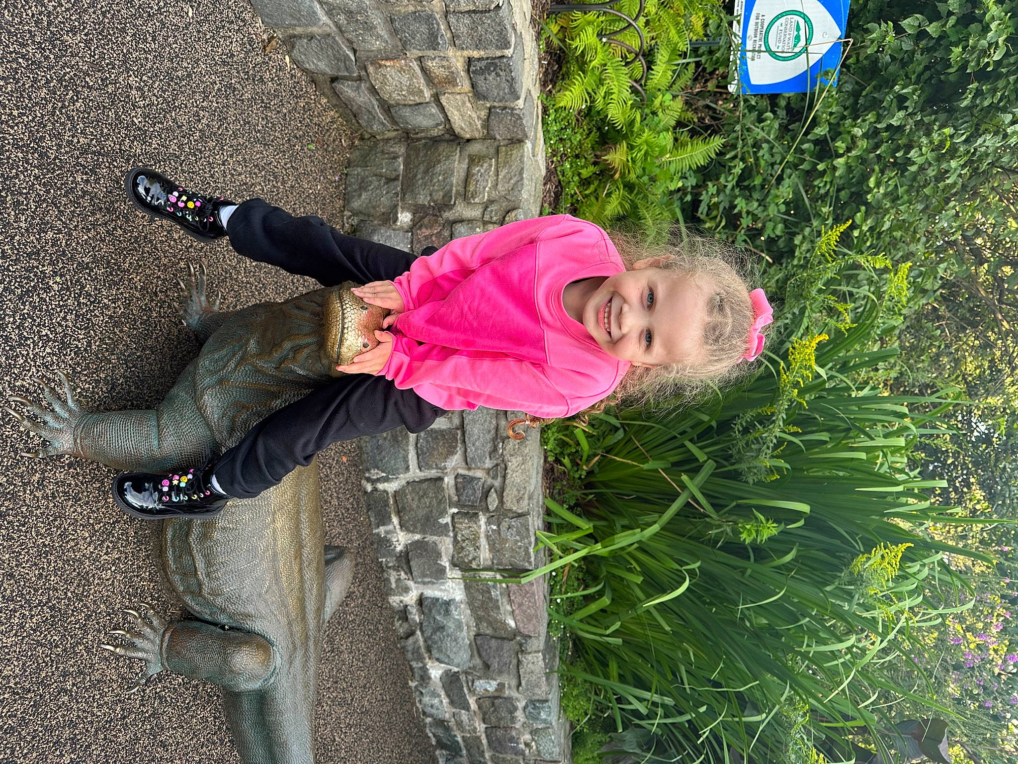 Angelina is registered to the contest to win money with this photo: boot, child, clothing, fun, grass, hat, joy, leisure, logo, outdoor_shoe, people_in_nature, person, plant, road_surface, shrub, toddler, traffic_sign, tree, walking_shoe
