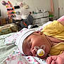 baby, bed, blanket, child, closeup, cute, hand, indoor, infant, newborn, nursery, pacifier, peaceful, person, resting, skin, sleeping, soft_lighting, white_hat, yellow_clothing