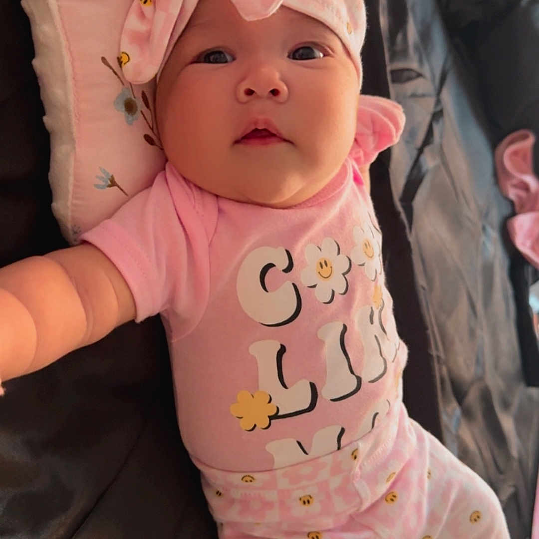 Denayt joined the competition — help win amazing prizes! baby, child, chubby_cheeks, couch, cozy, cute, fabric, face, headband, indoors, infant, lying_down, patterned_clothing, person, pillow, pink_clothing, portrait, reaching, smileys, soft_toys