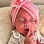 baby, child, closeup, cushion, cute, finger_on_lips, flower, headwear, indoors, infant, newborn, peaceful, pink_headwrap, portrait, resting, skin, sleepy, small_hands, soft_texture, white_clothing
