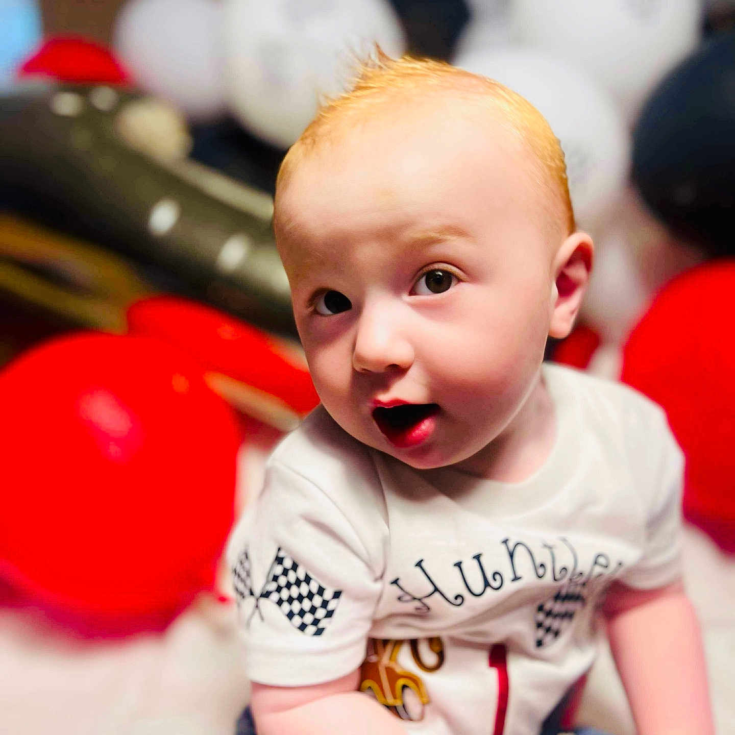 Huntley joined the competition — help win amazing prizes! baby, background, balloons, casual_clothing, celebration, child, curious, cute, expression, face, indoor, jeans, light, party, portrait, red_hair, shirt, sitting, toddler, young_child