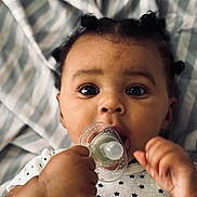 Jey-ïqa joined the competition — help win amazing prizes! baby, infant, pacifier, face, hand, onesie, star_pattern, blanket, striped_blanket, curious_eyes, closeup, cute, child, newborn, soft_lighting, portrait, skin, expression, lying_down, young_child