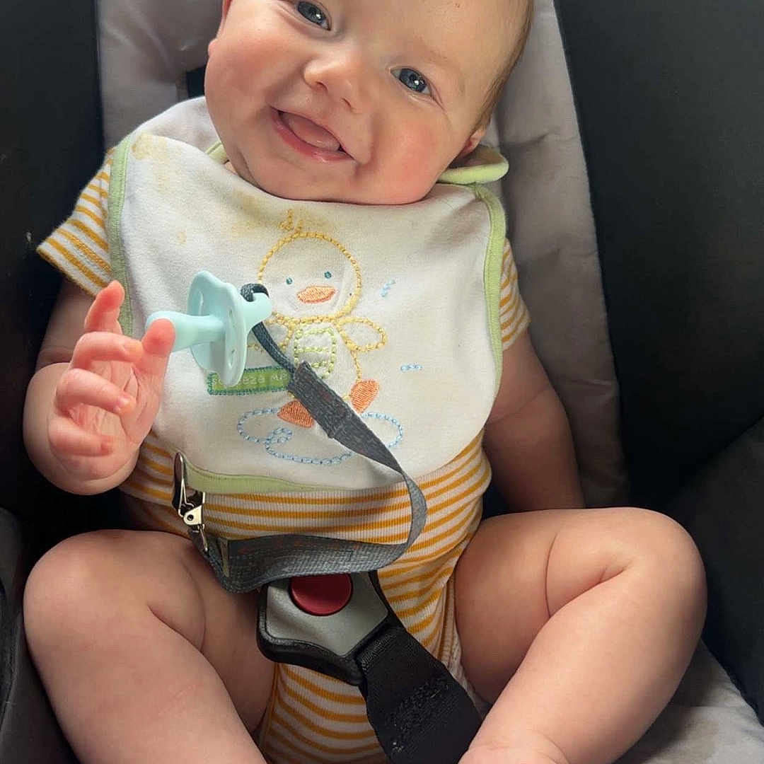Hezekiah is registered to the contest to win money with this photo: baby, baby_toys, barefoot, bib, car_seat, child, chubby_cheeks, closeup, comfort, cute, happy, indoor, infant, onesie, pacifier, person, portrait, seatbelt, smiling, striped_clothing