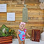 Elena is registered to the contest to win money with this photo: toddler, child, indoor, wooden_wall, romper, headband, pink_bow, shoes, floor, decor, plant, crate, macrame, flower, portrait, smiling, standing, baby, cute, happy