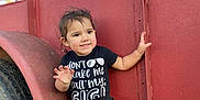Elena joined the competition — help win amazing prizes! toddler, child, smile, black_clothing, cowboy_boots, red_trailer, outdoor, daylight, grass, tire, metal_structure, sitting, playful, happy, face, person, young_child, nature, casual, funny_shirt