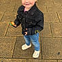 toddler, child, smiling, standing, outdoor, pavement, denim_jacket, jeans, toy, topknot, casual_clothing, footwear, cute, happy, person, young_child, playful, daylight, urban, fashion