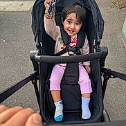 Khiyanshi joined the competition — help win amazing prizes! toddler, child, stroller, keys, smile, happy, outdoor, sidewalk, clothing, socks, person, seatbelt, black_stroller, hand, urban, pavement, cute, joyful, walking, baby