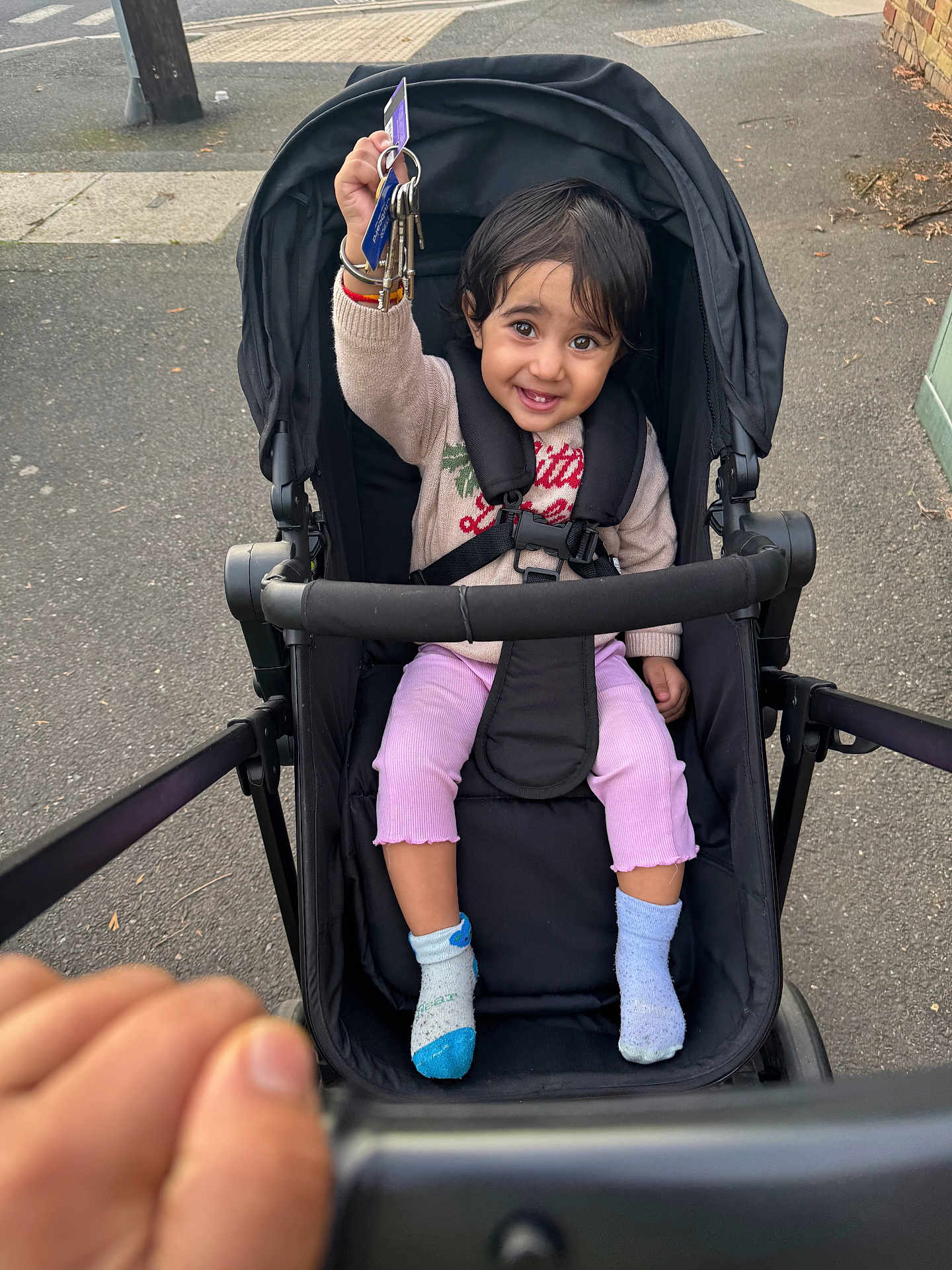 Khiyanshi joined the competition — help win amazing prizes! toddler, child, stroller, keys, smile, happy, outdoor, sidewalk, clothing, socks, person, seatbelt, black_stroller, hand, urban, pavement, cute, joyful, walking, baby