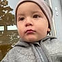 toddler, child, face, hoodie, beanie, window, reflection, tree, outdoor, portrait, person, video_call, technology, casual_clothing, expression, young_child, close_up, communication, indoor, adult
