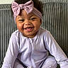 baby, child, infant, smiling, laughing, portrait, headband, bow, lavender_clothing, onesie, sitting, couch, indoor, home, curly_hair, dark_skin, happy, cute, facial_expression, photography
