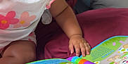 Leya participe au concours pour gagner de l'argent avec cette photo : toddler, child, toy, book, colorful, hand, face, indoor, cushion, clothing, curious, reading, purple, pink, white, play, baby, expression, seat, learning