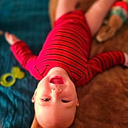 Levi is registered to the contest to win money with this photo: baby, child, smiling, red_clothing, striped_shirt, blanket, toy, blue_quilt, happy, face, head, lying_down, indoor, infant, person, cute, playful, warm, soft_texture, mouth_open