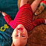 baby, child, smiling, red_clothing, striped_shirt, blanket, toy, blue_quilt, happy, face, head, lying_down, indoor, infant, person, cute, playful, warm, soft_texture, mouth_open