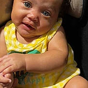 Royalty Griffin is registered to the contest to win money with this photo: baby, child, curly_hair, blue_eyes, yellow_outfit, sitting, hand_holding, cushion, seat, portrait, indoor, soft_light, cute, infant, smile, skin, person, closeup, young, happy