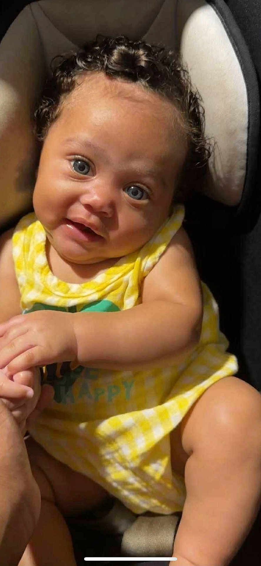 Royalty Griffin is registered to the contest to win money with this photo: baby, child, curly_hair, blue_eyes, yellow_outfit, sitting, hand_holding, cushion, seat, portrait, indoor, soft_light, cute, infant, smile, skin, person, closeup, young, happy