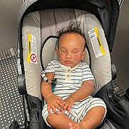 Truce Clarke is registered to the contest to win money with this photo: baby, car_seat, sleeping, infant, child, curly_hair, striped_clothing, hands, feet, cushion, elevator, metal, warning_label, modern, indoor, peaceful, relaxed, transportation, seat, person