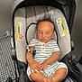 baby, car_seat, sleeping, infant, child, curly_hair, striped_clothing, hands, feet, cushion, elevator, metal, warning_label, modern, indoor, peaceful, relaxed, transportation, seat, person
