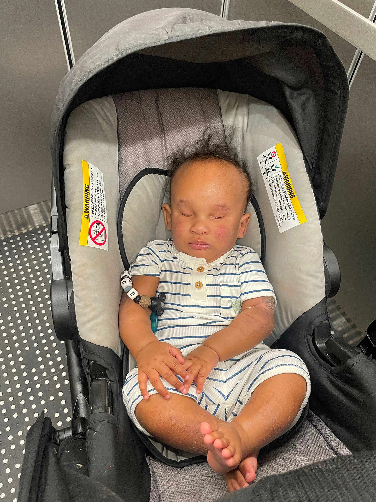 Truce Clarke is registered to the contest to win money with this photo: baby, car_seat, sleeping, infant, child, curly_hair, striped_clothing, hands, feet, cushion, elevator, metal, warning_label, modern, indoor, peaceful, relaxed, transportation, seat, person