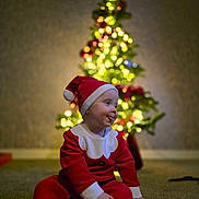 Cillian joined the competition — help win amazing prizes! child, toddler, santa_claus_costume, christmas_tree, holiday, festive, indoor, carpet, blurred_background, lights, decoration, red_clothing, hat, playful, smiling, cute, celebration, holiday_season, portrait, happy