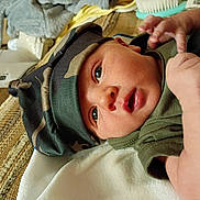 Bradlee joined the competition — help win amazing prizes! baby, infant, hat, camouflage, green_clothing, face, eyes, mouth, hand, skin, blanket, fabric, texture, lying_down, close_up, newborn, cute, indoors, soft_light, portrait