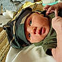 baby, infant, hat, camouflage, green_clothing, face, eyes, mouth, hand, skin, blanket, fabric, texture, lying_down, close_up, newborn, cute, indoors, soft_light, portrait