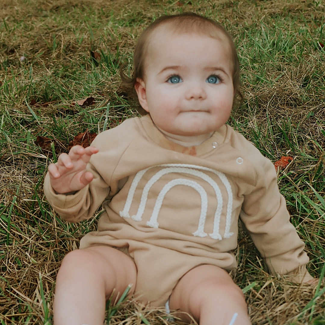 Iris is registered to the contest to win money with this photo: baby, bodypart, clothing, face, finger, footwear, grass, hand, head, lawn, pants, person, photography, plant, portrait, runningshoe, shoe, shorts, sitting, sneaker