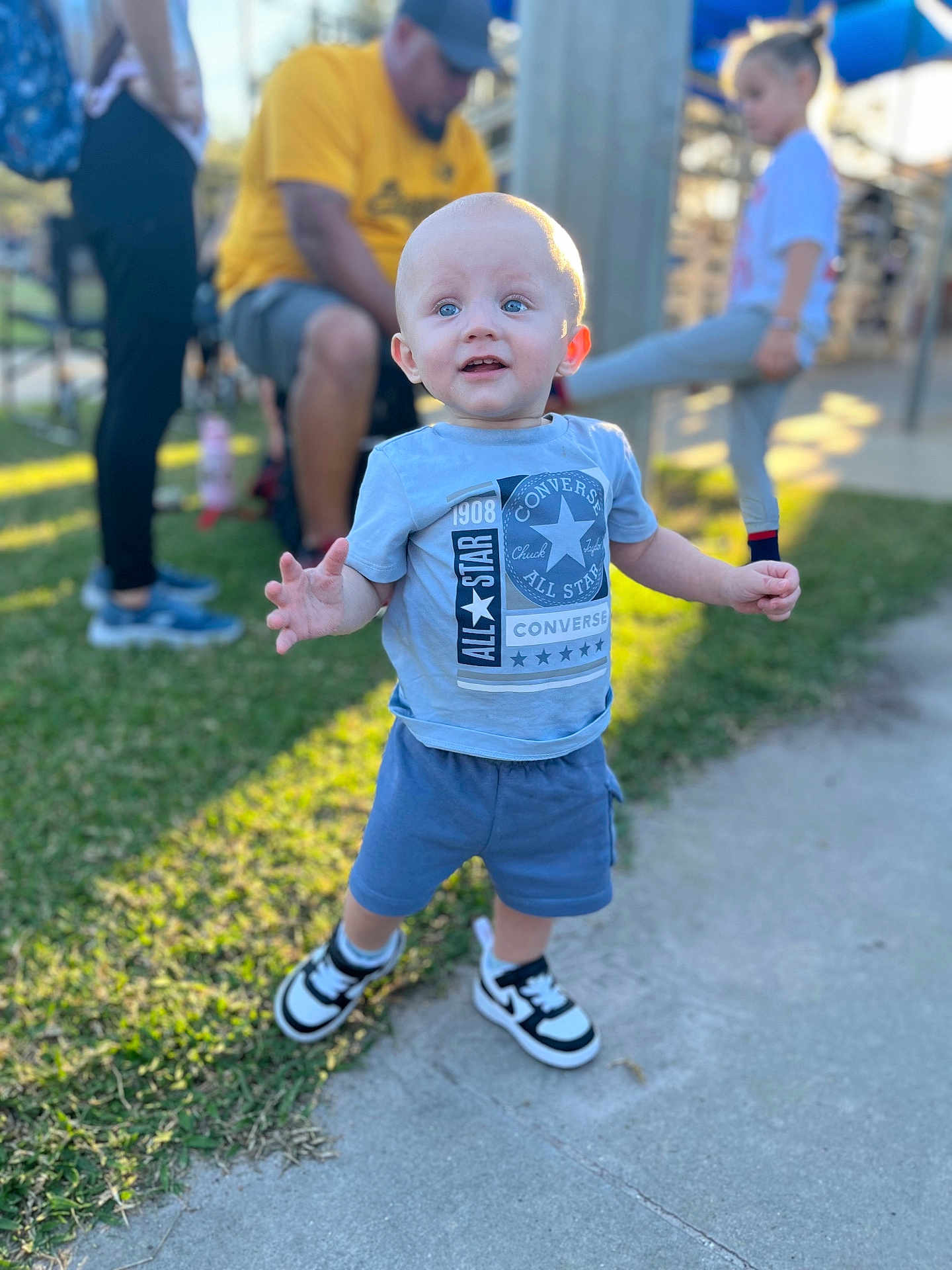 Ryder is registered to the contest to win money with this photo: blue_shirt, blurred_background, casual, child, clothing, daylight, grass, happy, hat, man, outdoor, park, people, person, playground, shorts, sidewalk, sneakers, toddler, yellow_shirt