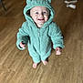 apparel, baby, barefoot, child, cute, eyes, face, fuzzy_texture, green_clothing, happy, hood, hoodie, indoor, infant, one_person, portrait, smiling, standing, toddler, wooden_floor